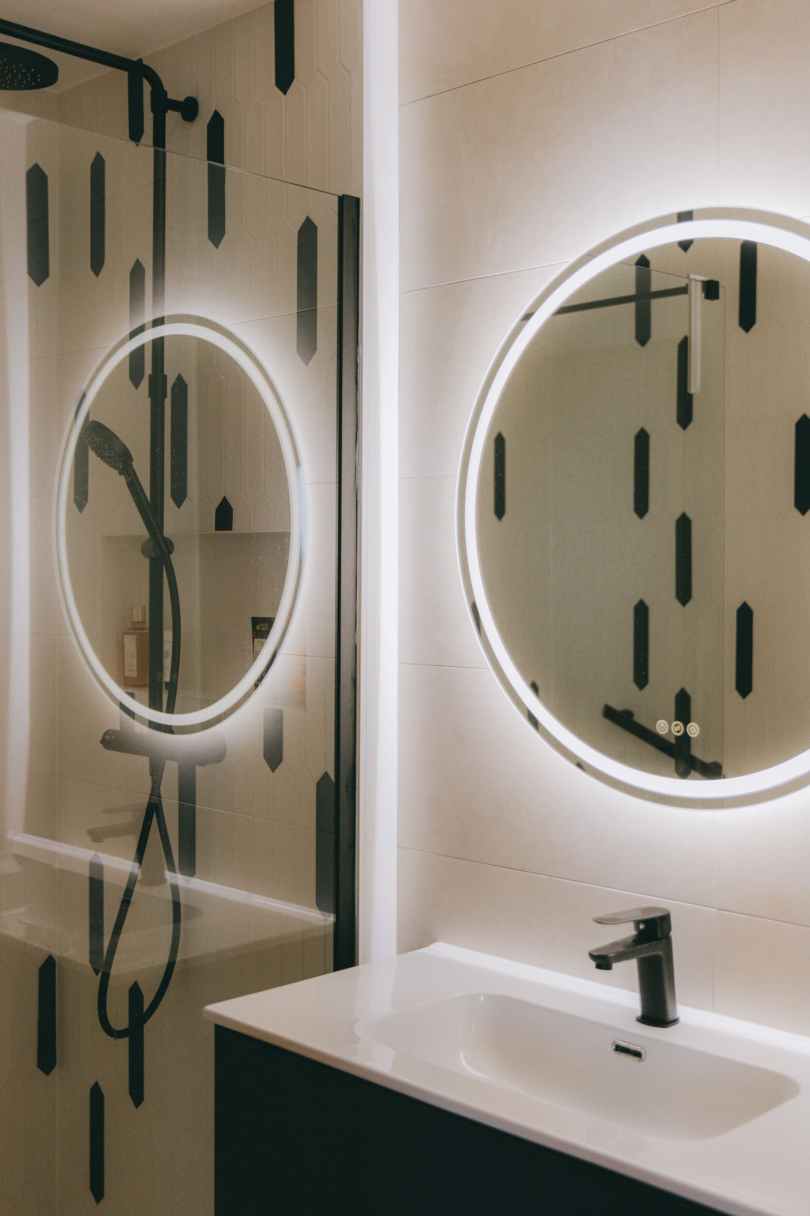 Salle de bain moderne avec miroir rond rétroéclairé et robinet noir – La Grande-Motte