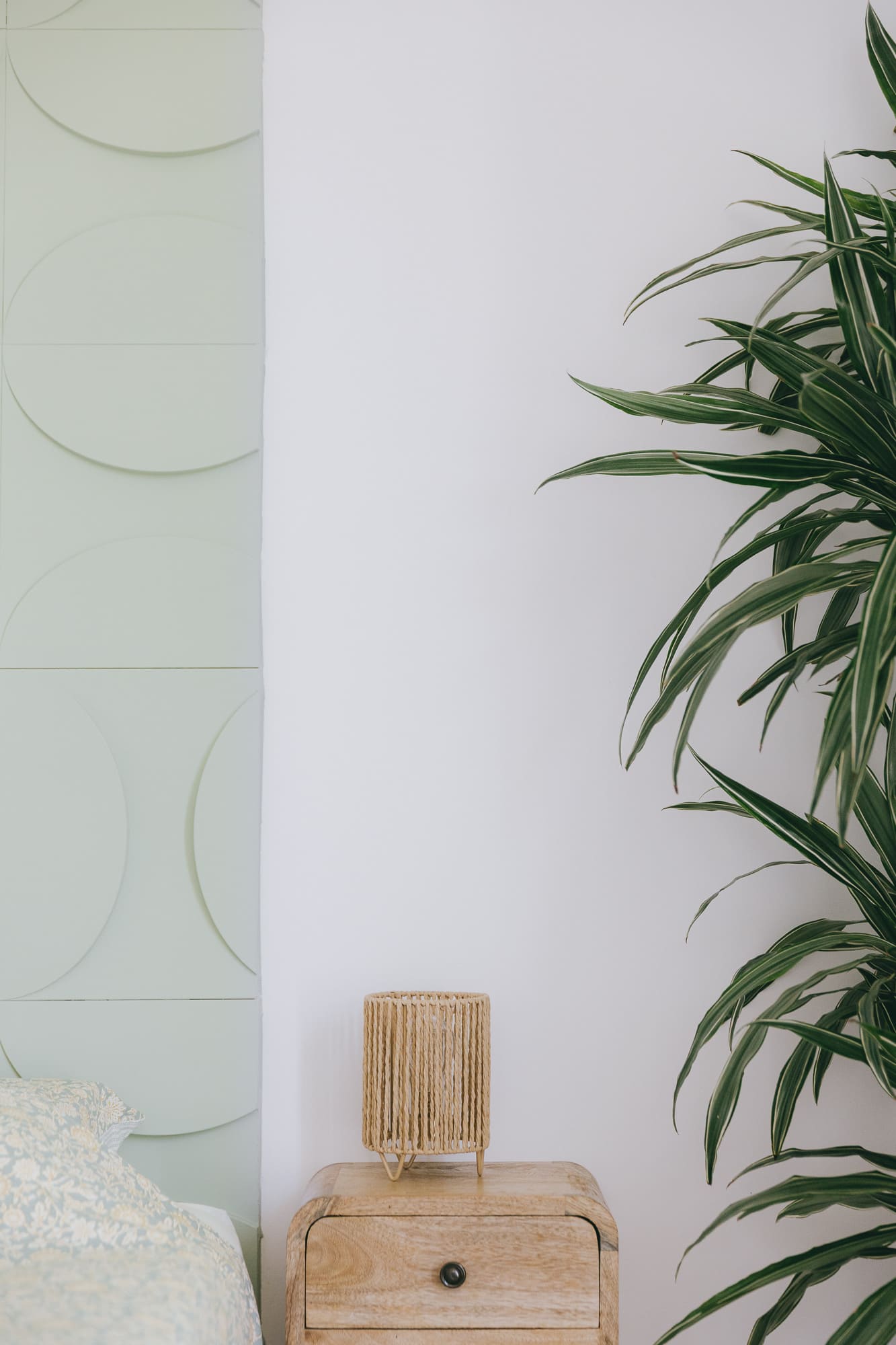 Détail de la chambre à coucher avec table de chevet en bois de manguier, lampe tressée et mur décoratif vert d'eau