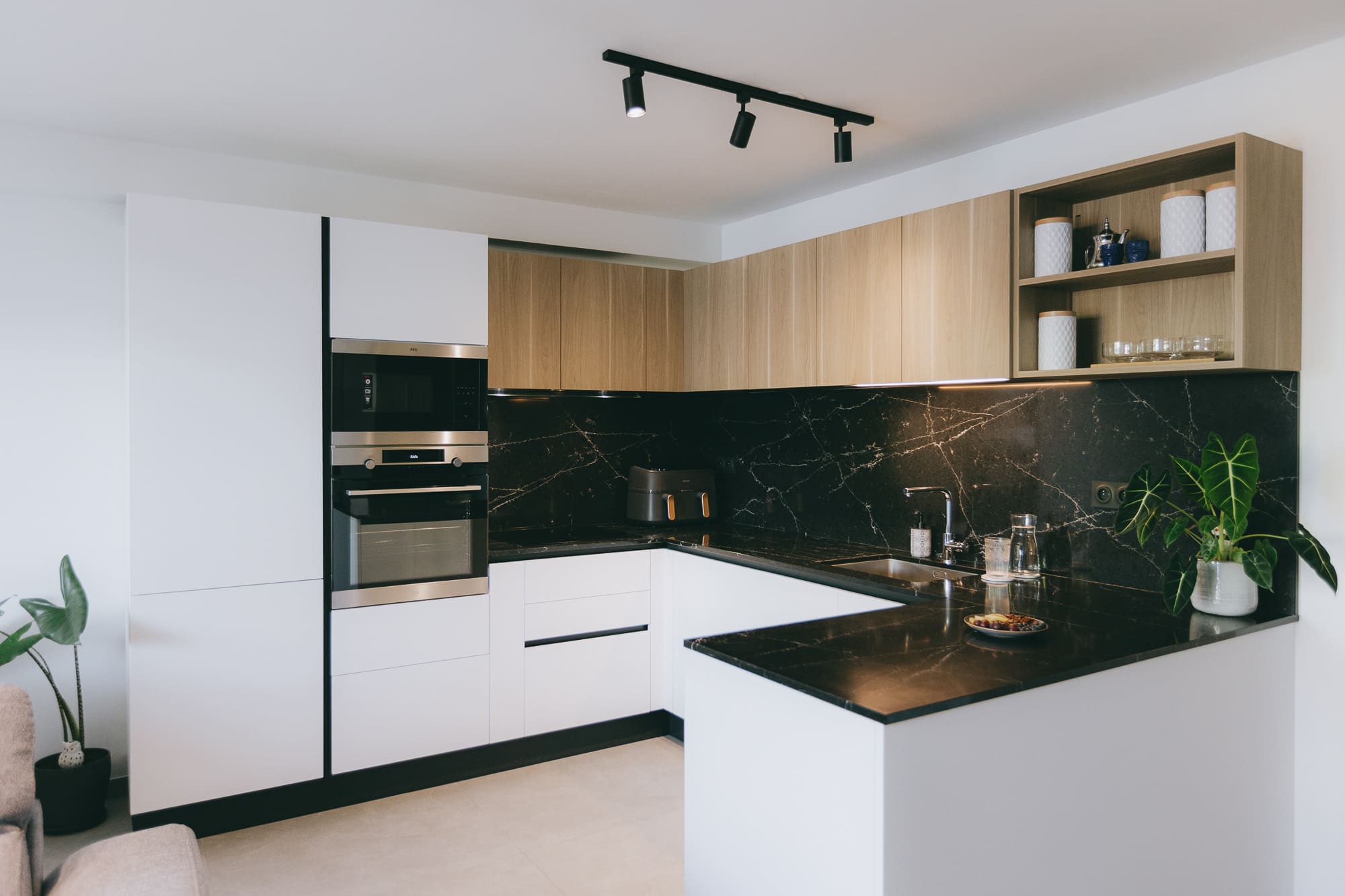 Cuisine équipée moderne avec façades blanches, plan de travail noir et meubles hauts en bois, réalisation agence Dugas