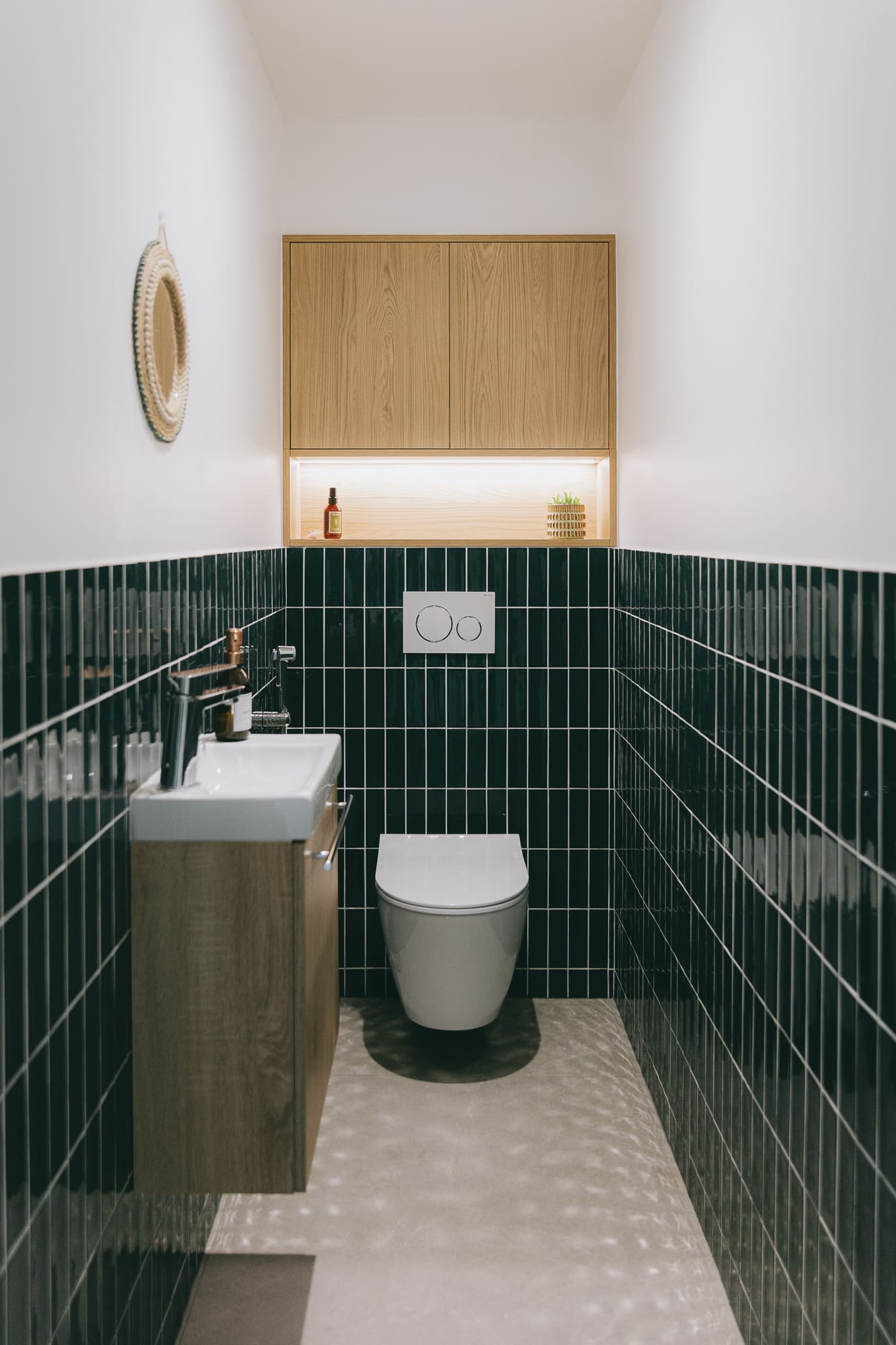 Aménagement des toilettes avec carrelage mural vertical noir brillant, lave-mains en bois et WC suspendu