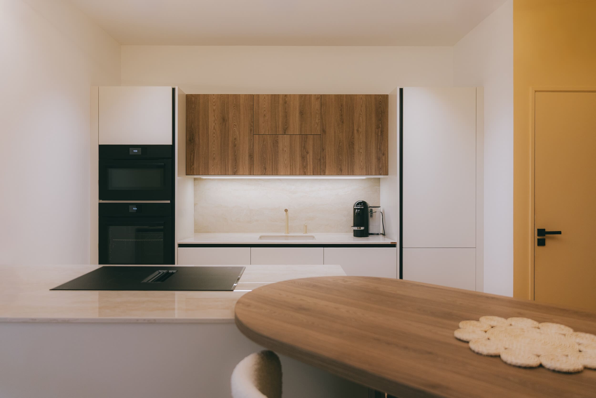 Cuisine sur mesure alliant façades blanches, bois naturel, plan de travail en pierre et électroménager intégré dans un projet de rénovation