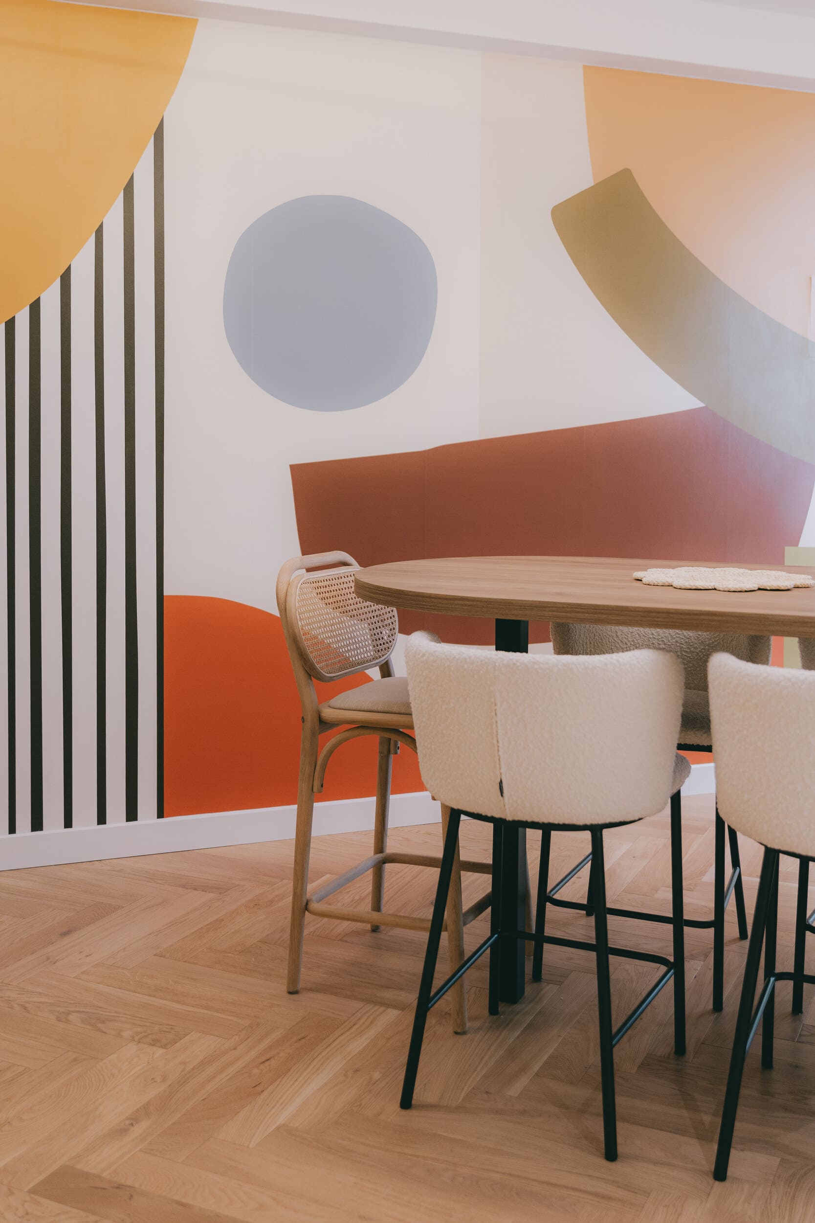 Espace repas chaleureux avec mobilier design, parquet en chevrons et fresque murale sur mesure dans un projet d'architecture intérieure