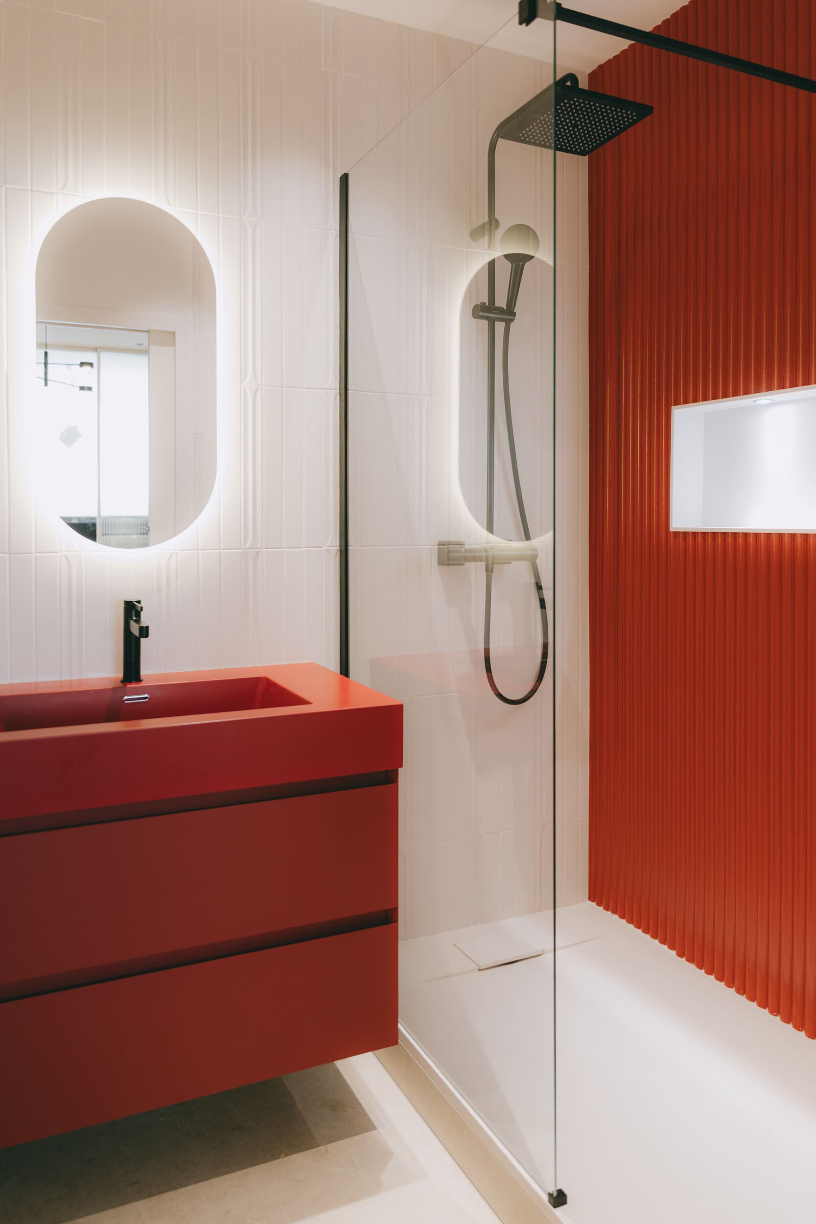 Salle de bains design avec douche à l'italienne, meuble vasque rouge, faïence texturée et robinetterie noire dans un projet de rénovation
