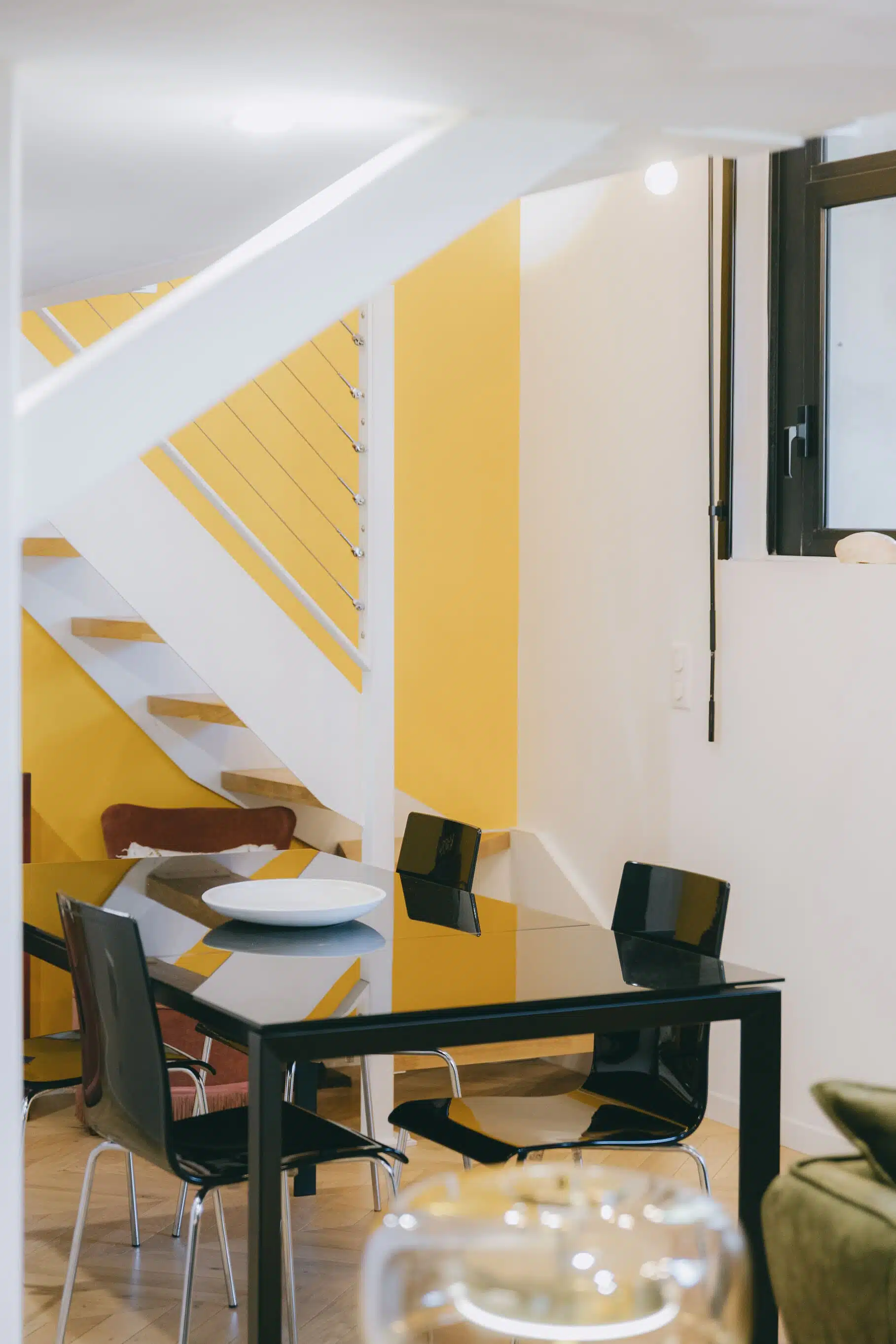 Coin salle à manger sous l'escalier, table noire et mur jaune