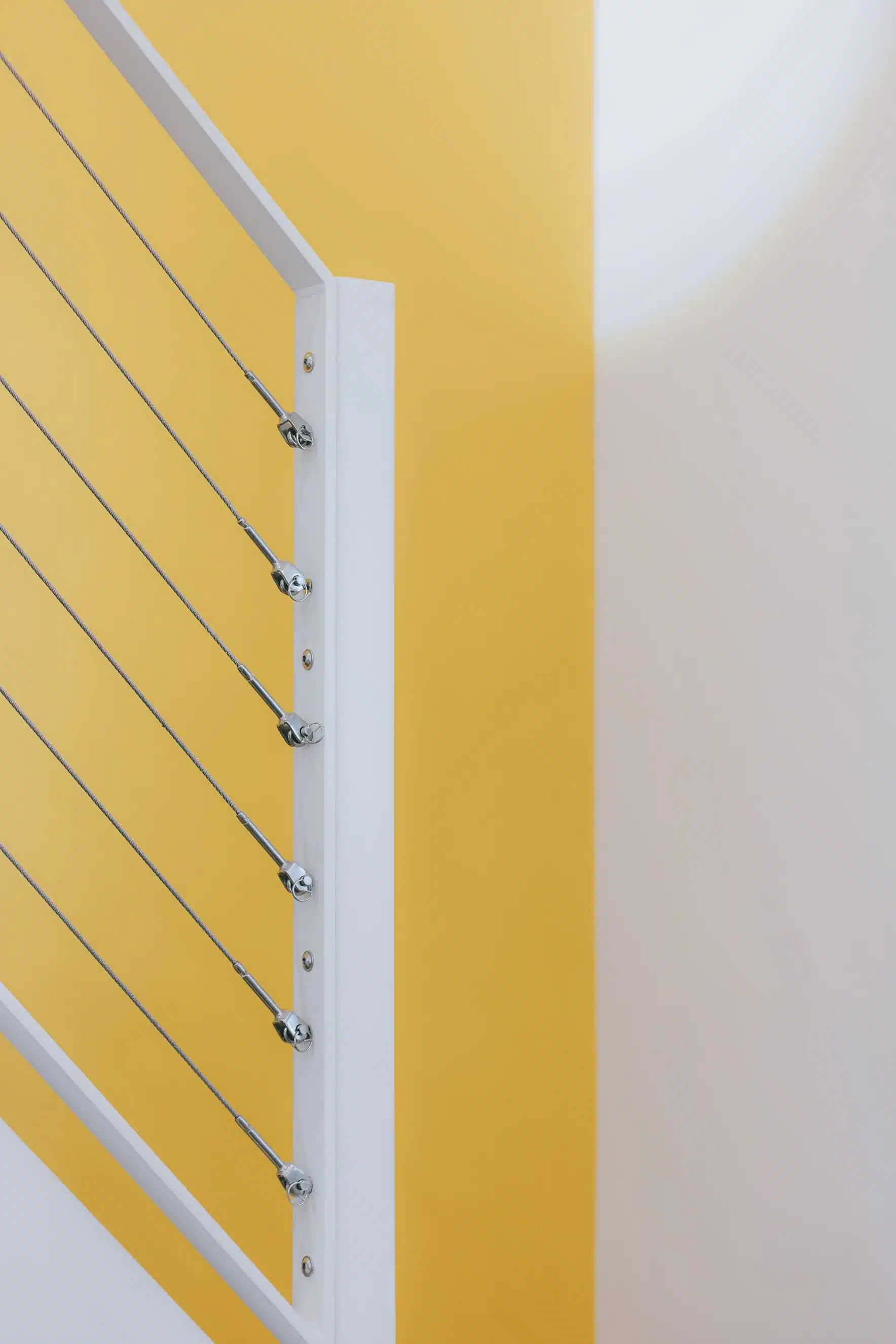 Détail du garde-corps à câbles inox devant un mur jaune