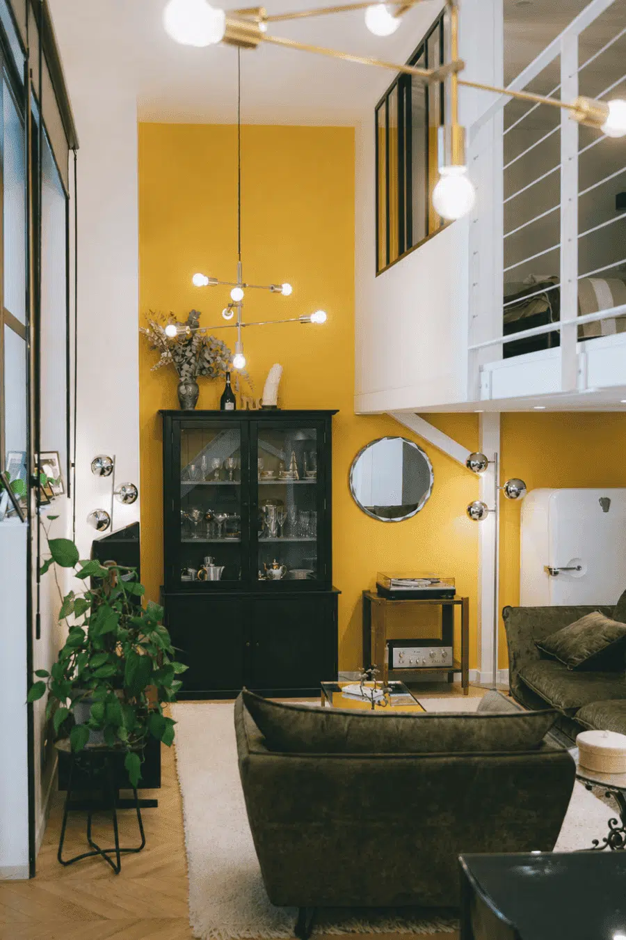 Séjour double hauteur avec mezzanine, mur jaune et buffet vitré noir